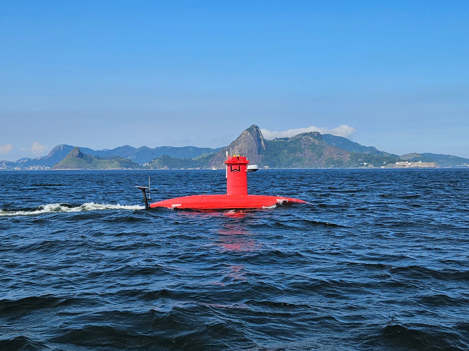 Exail DriX uncrewed survey vessel under way with coastal mountains behind