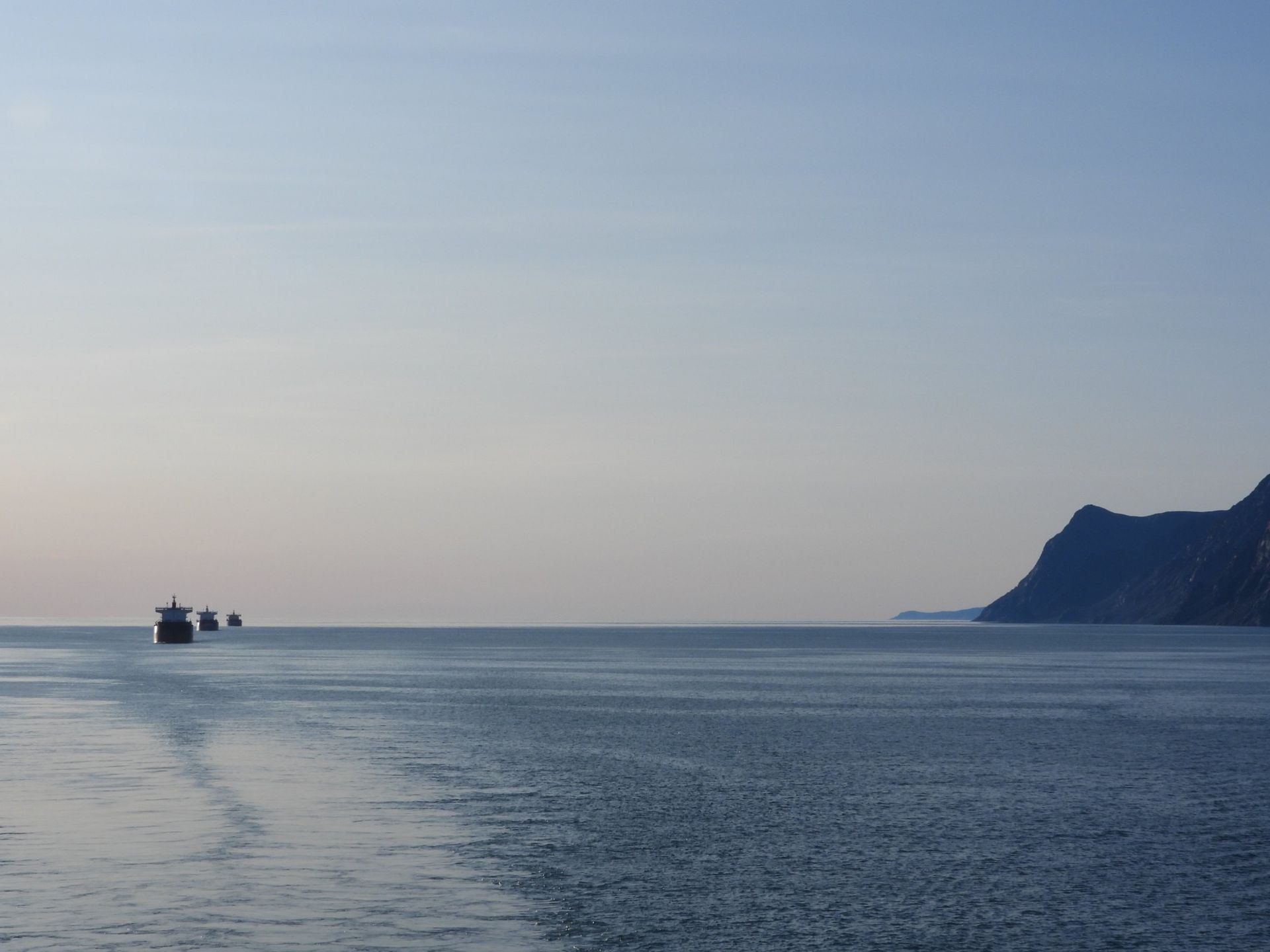 Vessels in line along a rocky coast at dusk